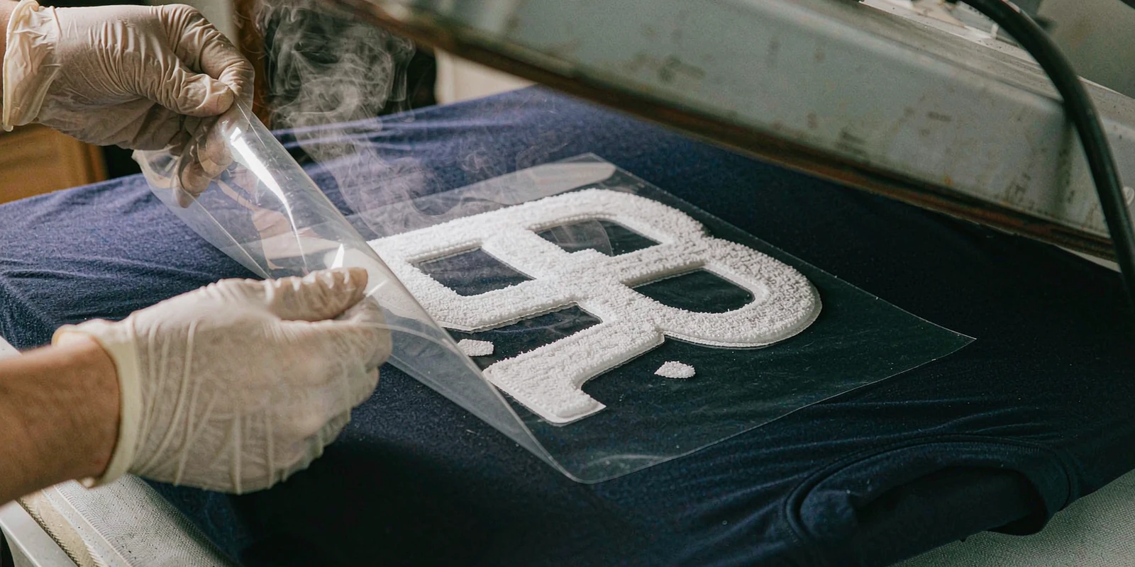 Worker peeling carrier film from a freshly heat pressed flocked number on a navy jersey Worker peeling carrier film from a freshly heat pressed flocked number on a navy jersey